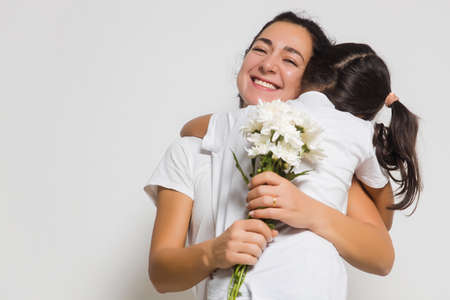 Girl child daughter hugging happy mom, congratulating with bouquet during Womens or Mothers Day. Copy space for adの写真素材