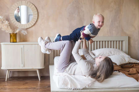 Joyful young mother hold son toddler imitate plane fly having fun play in funny game lying on bed in cozy homeの写真素材