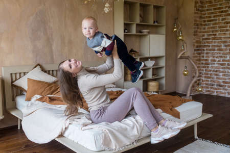Joyful young mother hold son toddler imitate plane fly having fun play in funny game lying on bed in cozy homeの写真素材