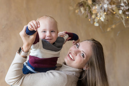 Joyful beautiful caucasian mother holding in hands laughing cute child son. Young mum cuddling kid boy. Happy motherhoodの写真素材