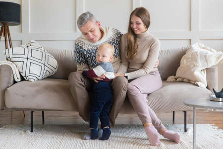 Happy young family with toddler son on grey apartment wall background with copy space. Rental, moving, mortgage conceptの写真素材