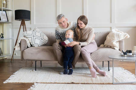 Happy young family with toddler son on grey apartment wall background with copy space. Rental, moving, mortgage conceptの写真素材