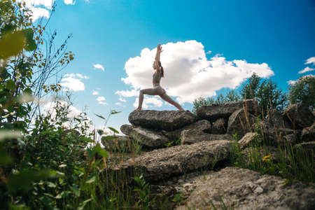 Woman practicing Warrior yoga pose outdoors over sunset sky background.の写真素材