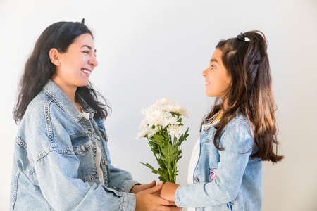 Happy young mother getting flowers from daughter little girl kid during mothers day. Tender moment of motherhoodの写真素材
