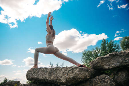 Woman practicing Warrior yoga pose outdoors over sunset sky background.の写真素材