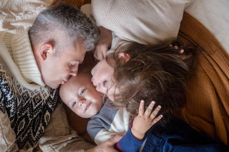 Parents kissing cute smiling little kid son head lying on bed. Mom dad with child, top view portrait. Tender momentの写真素材