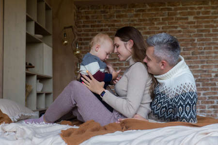 Happy father and mother holding little kid boy son in hands sitting on bed at cozy home. Tender parenthood momentの写真素材