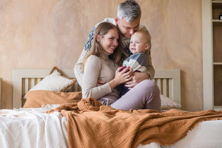 Happy father and mother holding little kid boy son in hands sitting on bed at cozy home. Tender parenthood momentの写真素材