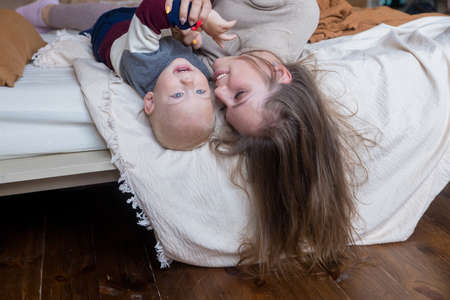 Smiling young mother resting on comfortable bed with cute little kid son toddler together at home. Motherhood conceptの写真素材