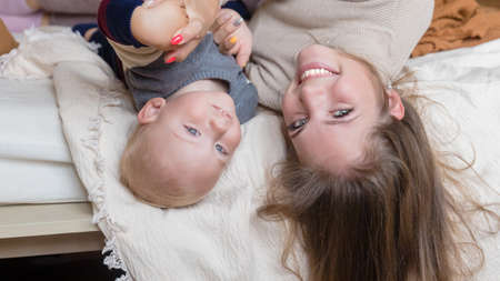 Smiling young mother resting on comfortable bed with cute little kid son toddler together at home. Motherhood conceptの写真素材