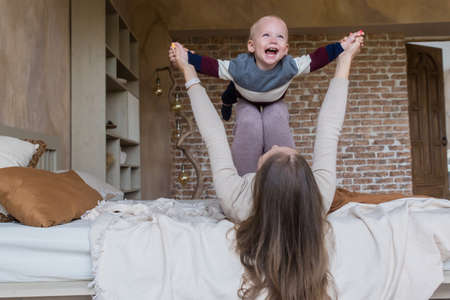 Loving young mother have fun play with happy little toddler son together lying on bed on family weekendの写真素材