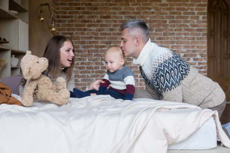 Affectionate young family having fun playing with little son on bed at home. Happy parenthood conceptの写真素材