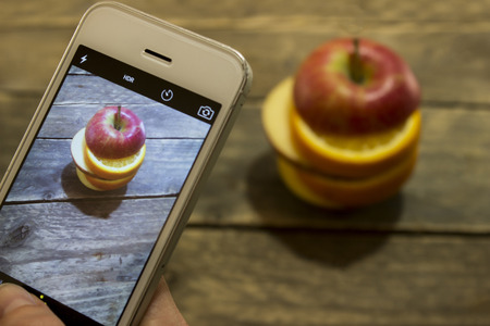 Girl takes a picture of a sliced apple on a wooden table .