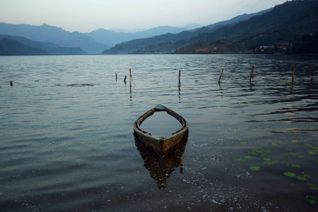 Old wooden boat reflected in water on the Phewa lake in Pokhara. Calm and relax morning mood. Annapurna mountain range on a backgroundの写真素材