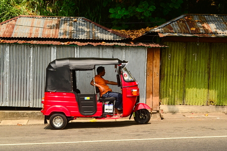Kadugannawa, Sri Lanka - February, 2014: Tuk tuk driver waiting for passengers in his  three wheeler red auto rickshaw.のeditorial素材