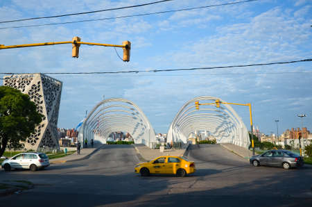 Cordoba, Argentina - January, 2020: Yellow taxi car crossing intersection on green traffic light near Puente del Bicentenario (Bicentenary Bridge) near Centro Civico del Bicentenario buildingのeditorial素材