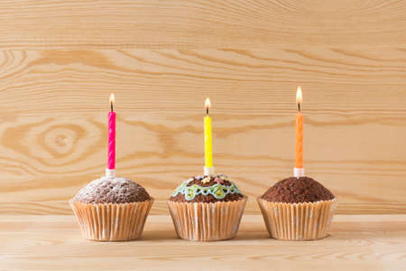 three homemade muffins, cakes with candles on a wodden backgroundの写真素材