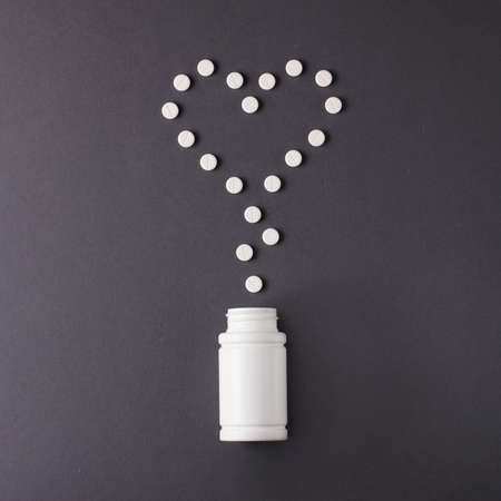 heart pills and white jar for pills on a gray backgroundの写真素材