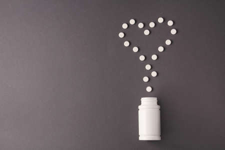 heart pills and white jar for pills on a gray backgroundの写真素材