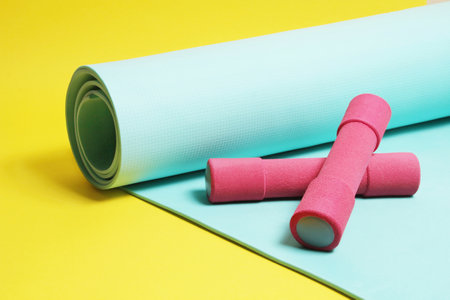 Fitness items dumbbells and exercise mat on a yellow backgroundの写真素材