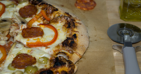 Pizza with pepperoni, mushrooms, mozzarella and tomato sauce. Pizza on the wooden table In the frame is half a pizza and a silver pizza cutterの写真素材