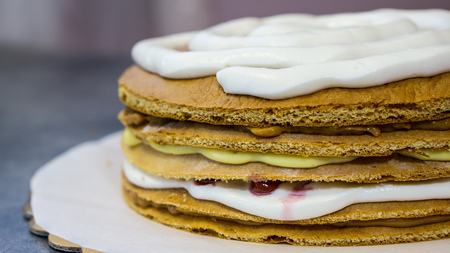 Sponge cake with white cream, a protruding cream between biscuit cakes, on a stone tableの写真素材