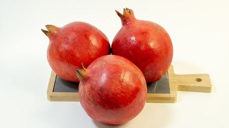Bright juicy pomegranate fruit, white background, in the photo the following three fruits are placed with a triangle, on the kitchen board, close-upの写真素材
