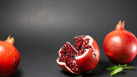 Black background, in the photo there are three pomegranates fruit in the middle of the rosewood and pomegranate grains are visible, green foliage is also on the rightの写真素材