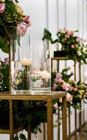 vases with burning candles on the table against the background of flowers, copy spaceの写真素材