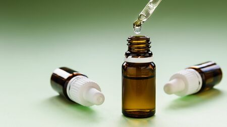 cosmetology, a row of glass bottles with pipettes and hyaluronic acid inside on a green background