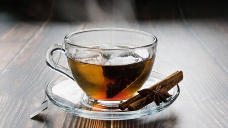 transparent cup on a saucer with a tea bag, cinnamon sticks and anise on the tableの写真素材