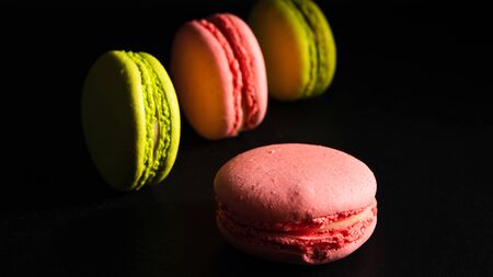sweets advertising concept, french dessert - pink and pistachio macaroons on a black background, close-upの写真素材