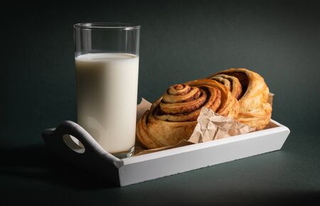 cinnamon roll and a glass of milk on a dark background