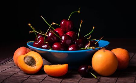 still life, blue plate with cherries and apricots on a dark backgroundの写真素材