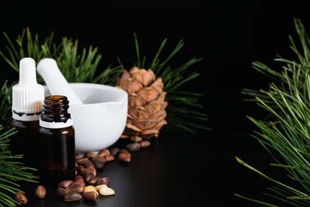 natural production concept, pine cone with nuts, glass bottle and mortar on a black backgroundの写真素材