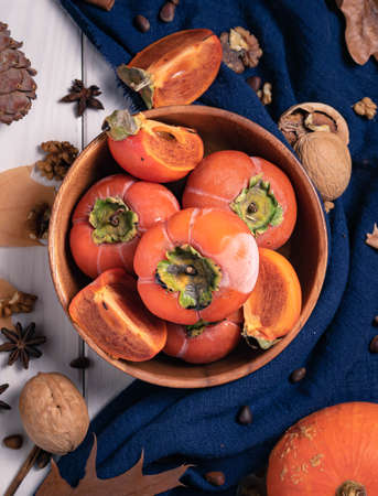 gifts of autumn, top view, ripe persimmons in a wooden bowl on a background with nuts, leaves and a...