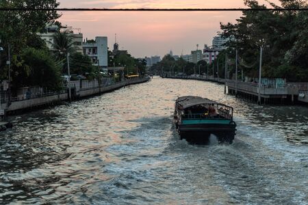 View from the bridge to the canals of Bangkok with a passenger boat and lots of wiresの写真素材