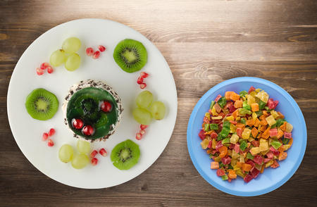 dessert of cake and fruit (grapes, kiwi, pomegranate) on a wooden background. dessert on a plate top viewの写真素材
