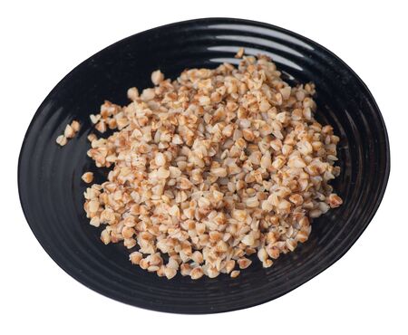 Buckwheat in a black plate isolated on white background. Buckwheat top side view. Healthy food.の写真素材