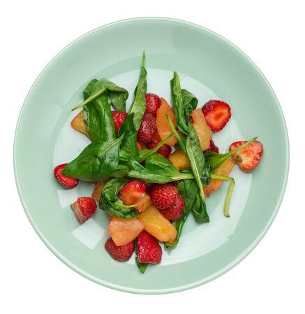 salad with strawberries, pineapple and spinach on a light green  plate. fruit vegetarian salad isolated on white background. vegan salad top viewの写真素材