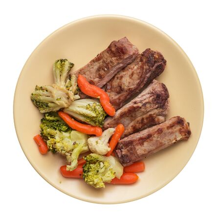 grilled pork ribs with broccoli cabbage, carrots and garlic on a light brown  plate. fried pork ribs with vegetables on a white background. hearty rustic food top viewの写真素材