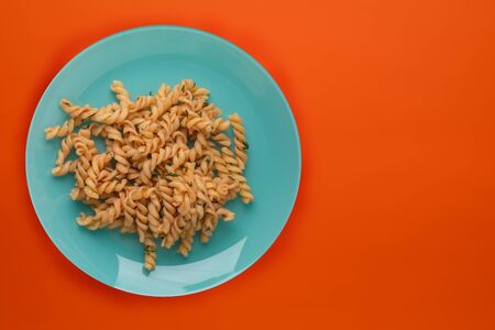 pasta on a plate cyan color in tomato sauce on a background of titanium color. Mediterranean food on an orange background. healthy foodの写真素材