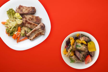 fried pork ribs with broccoli, carrots and garlic on a white plate. fried pork ribs with vegetable salad on a red background. hearty rustic food top view.flat layの写真素材