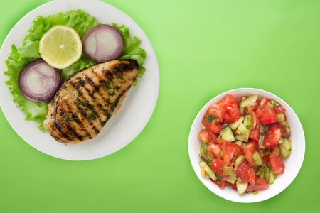  grilled chicken with vegetables lemon, salad, onion) on a lime background. grilled chicken fillet on a plate in a vegetable salad top view.flat layの写真素材