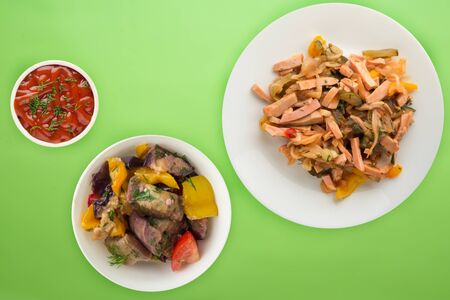 Berlin salad on a white plate with vegetablie salad on a lime background. Salad from sausage, cucumber, pepper top view .の写真素材
