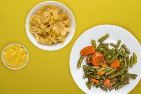 Green beans with garlic carrots on a white plate on a yellow background. green beans with carrots with vegetable vegetarian salad and sauce top view. healthy vegetarian food.flat layの写真素材