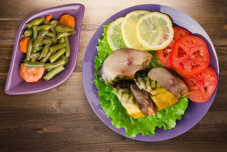 smoked mackerel on purple plate with vegetable salad top view. mackerel with lemon and tomato on brown wooden backgroundの写真素材