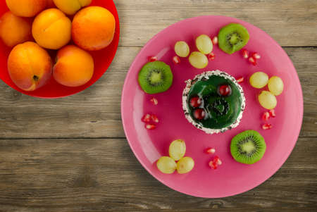 dessert of cake and fruit grapes, kiwi, pomegranate on a wooden background. dessert with fruits on...