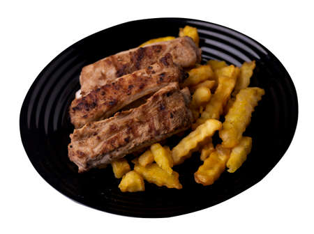 grilled pork ribs with french fries on black plate. pork ribs with french fries on a white background. ribs with potatoes top side viewの写真素材