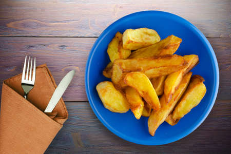fry potatoes on purple wooden background. fry potatoes on dark blue plate with fork and knife top viewの写真素材